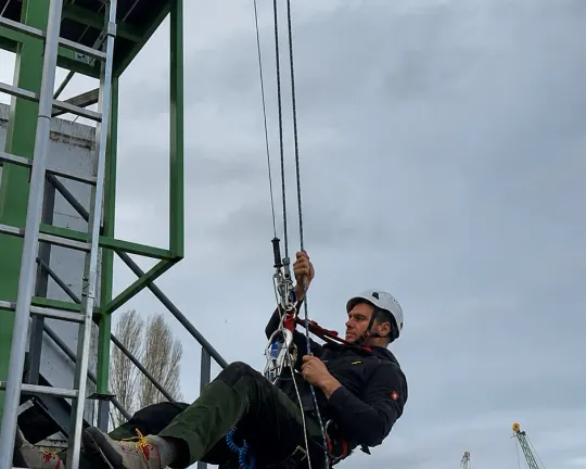 Курсист се спуска на въже покрай стълбата на учебната кула.